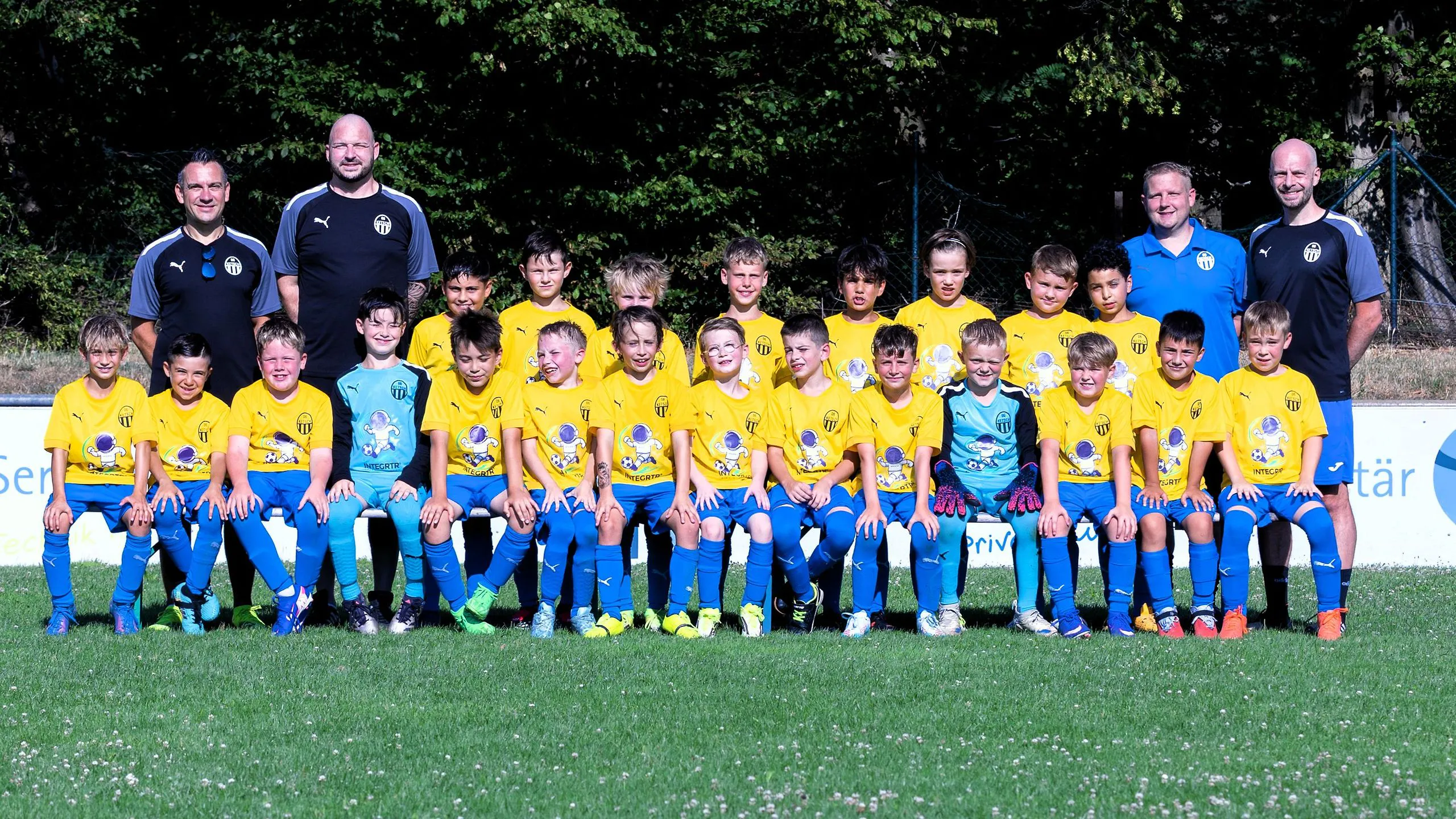 Nachwuchsmannschaft in gelben Trikots und blauen Hosen in zwei langen Reihen vor der Werbebande, an beiden Enden stehen insgesamt vier Trainer